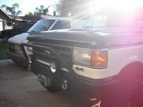 1991 Ford Bronco - Front view of a 1991 Ford Bronco equipped with a winch and bull bar, parked next to another vehicle.