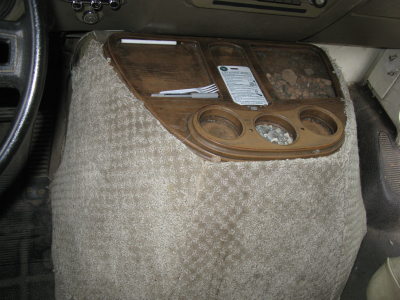 1991 Ford Bronco - The interior console of a vehicle shows a tray with cutlery and a document, along with cup holders.