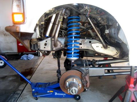 1996 Ford Bronco - Close-up of a vehicle's front suspension system, showing modified components and a bright blue coilover shock absorber.