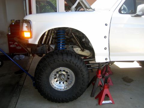 1996 Ford Bronco - Front suspension of a 1996 Ford Bronco, a large off-road tire and a prominent blue coilover shock absorber.