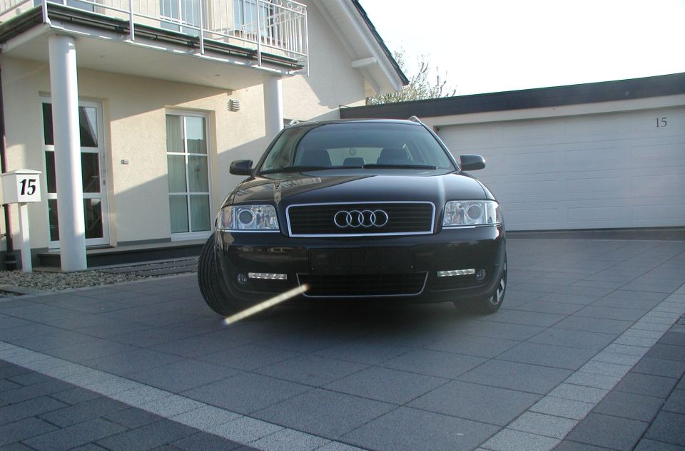 Front view of a black Audi A6 parked in a driveway in front of a house and garage