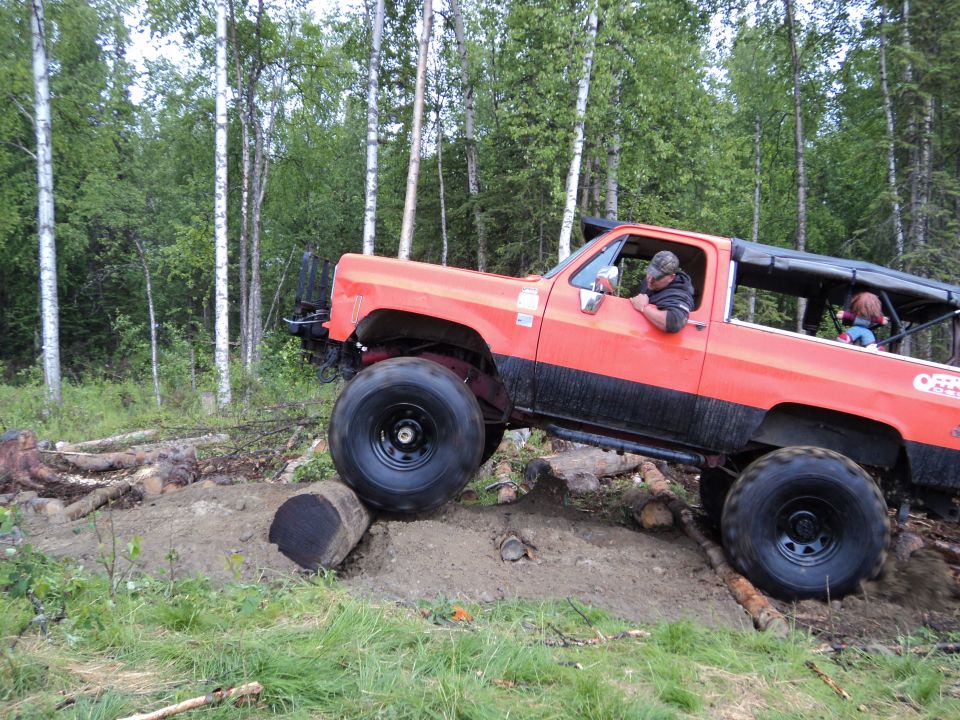 Orange 1990 Chevrolet Suburban off-roading over logs