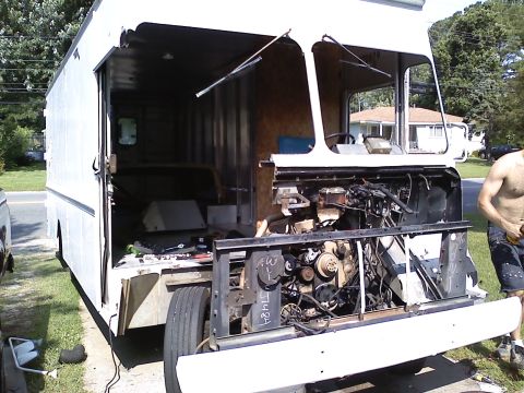 1990 Ford Bronco - A white step-van box truck being dismantled in a driveway, with the windshield, grille and front sheet metal stripped away to expose the en…