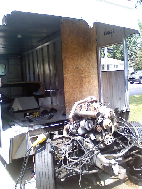 1990 Ford Bronco - A gutted white step-van marked "B20879" with the cab sheet metal and doghouse removed, exposing a dusty V-engine with intake tubing, altern…