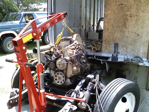 1990 Ford Bronco - An engine is being removed from a vehicle using a red engine hoist, with a blue Ford Bronco visible in the background.