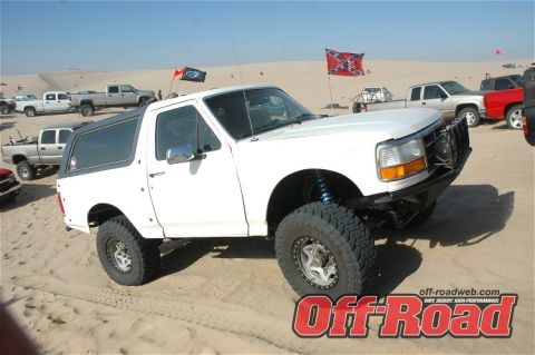1984 Ford Bronco - A white Ford Bronco is modified for off-road use and parked in the sand with other vehicles.