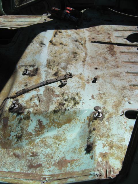 1978 Ford Bronco - The interior floor of a vehicle shows significant rust and wear, with exposed mounting hardware and wiring.