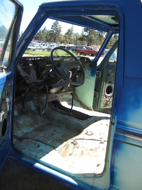 1978 Ford Bronco - The interior of a blue vehicle is visible with doors open, revealing a stripped dashboard and floor. Other vehicles are parked in the backg…