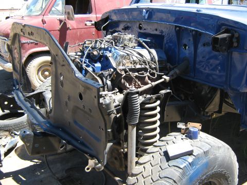 1978 Ford Bronco - The engine and front suspension components are exposed on a disassembled truck, with another vehicle visible behind it the background.