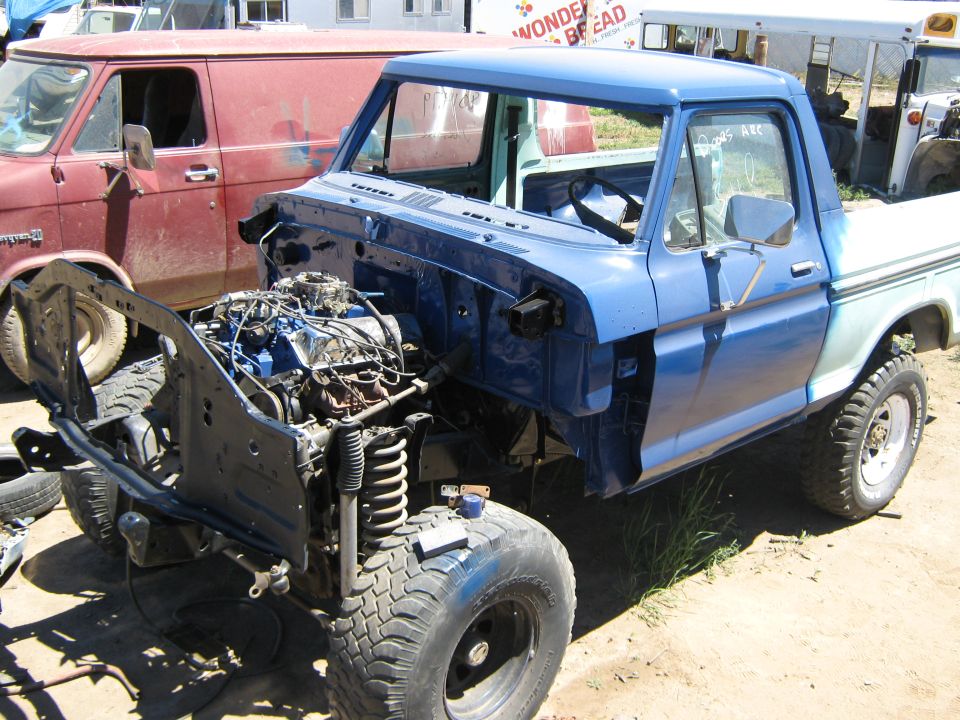 Blue pickup truck missing engine and front clip, parked next to a red van