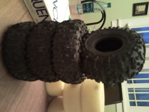 1989 Ford Bronco - Four off-road tires are shown stacked on a table, with a water bottle and box in the background.