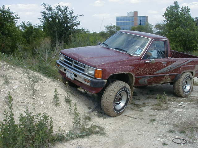 Muddy maroon lifted Toyota pickup flexing on a dirt berm