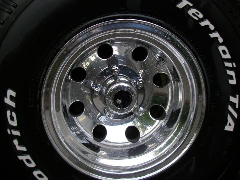 1990 Ford Bronco - Close-up of a polished chrome eight-slot wheel wet with water droplets, mounted with a BFGoodrich All-Terrain T/A raised-white-letter tire.…