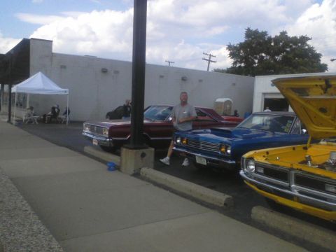 1960 Ford Falcon - Three muscle cars are parked in a row outside a building, with one having its hood up.