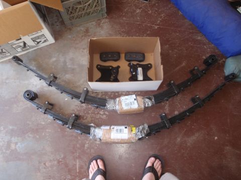 1994 Ford Bronco - Leaf springs and suspension parts laid out on a floor, with boxes in the background.