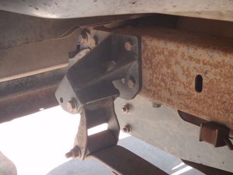 1994 Ford Bronco - Close-up view of a suspension bracket attached to a heavily rusted vehicle frame, showing the leaf spring.