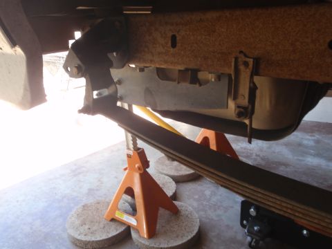 1994 Ford Bronco - The underside of a vehicle is shown, supported by jack stands, with visible rust on the frame components.