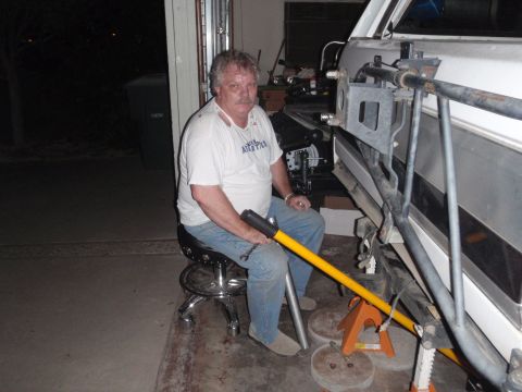 1994 Ford Bronco - A man sits on a stool, holding a yellow tool, while working on the suspension of a vehicle supported by jack stands.