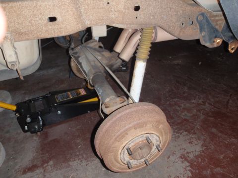 1994 Ford Bronco - Rear axle assembly with drum brake and shock absorber, supported by a floor jack.