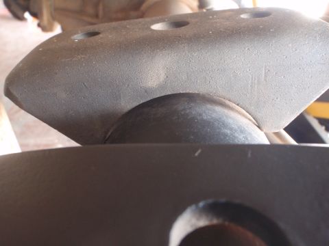 1994 Ford Bronco - Extreme underbody close-up of a dark cast-metal suspension/axle component with three drilled bolt holes across its top edge and a rounded b…