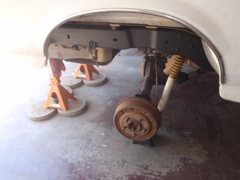 1994 Ford Bronco - The rear suspension and axle of a white vehicle are elevated on jack stands, revealing a rusty drum brake assembly.