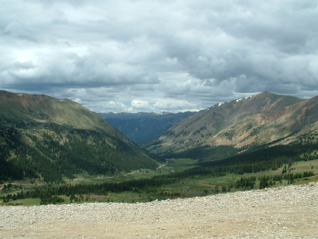 Mountain valley view under heavy gray clouds from a high gravel overlook
