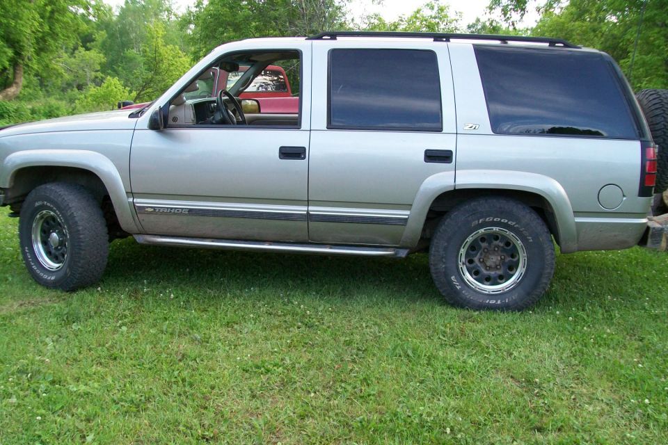 Silver 2000 Chevrolet Tahoe parked on grass, another red vehicle visible through the driver's side window