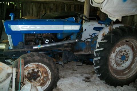 2000 Chevrolet Tahoe - A blue and white tractor is seen from the side, parked inside a wooden structure with other items around it.