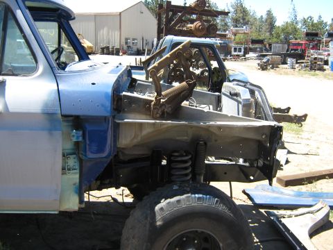 1978 Ford Bronco - This blue truck chassis is missing its front end, revealing the engine and suspension components. Another vehicle is visible in the backgro…