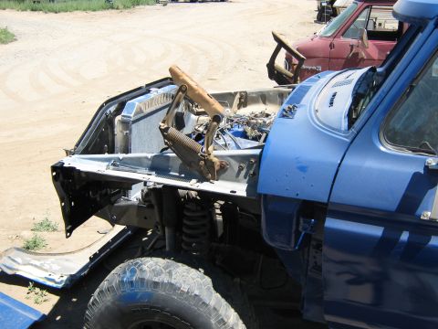 1978 Ford Bronco - A blue truck sits in a junkyard with its hood open, revealing the engine compartment.