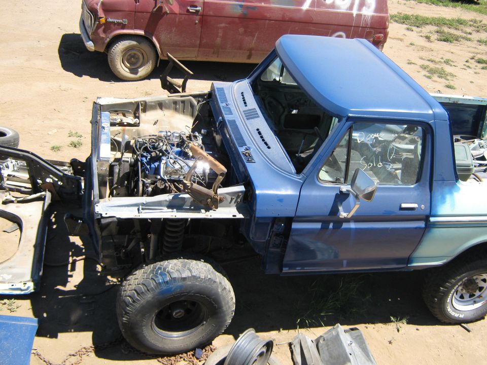 Blue pickup truck with engine exposed, showing front view and a red truck behind it