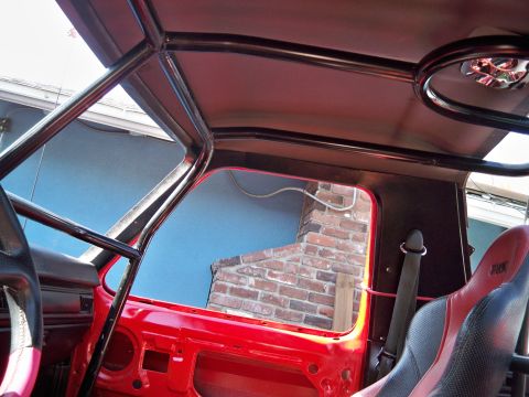 1985 Ford Bronco - Interior view of a red vehicle with a roll cage and racing seat, showing exposed door panel.