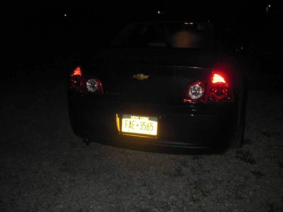 Rear view of a dark Chevrolet sedan with New York license plate FAE-3565, illuminated at night