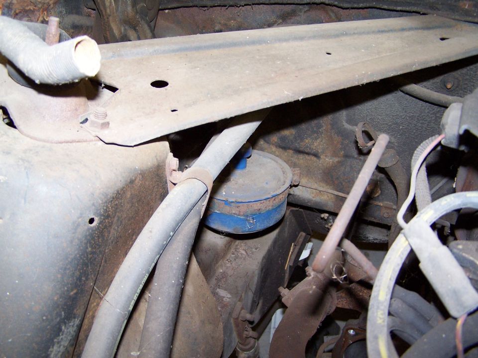 Engine bay with hoses, a blue-capped filter, and rusty metal components