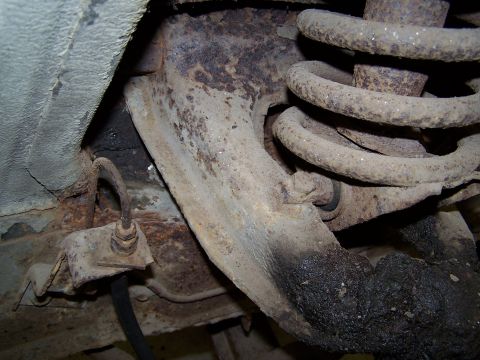 1972 Ford Mustang - Close-up of heavily rusted suspension components, including a coil spring and control arm, with a brake line visible.