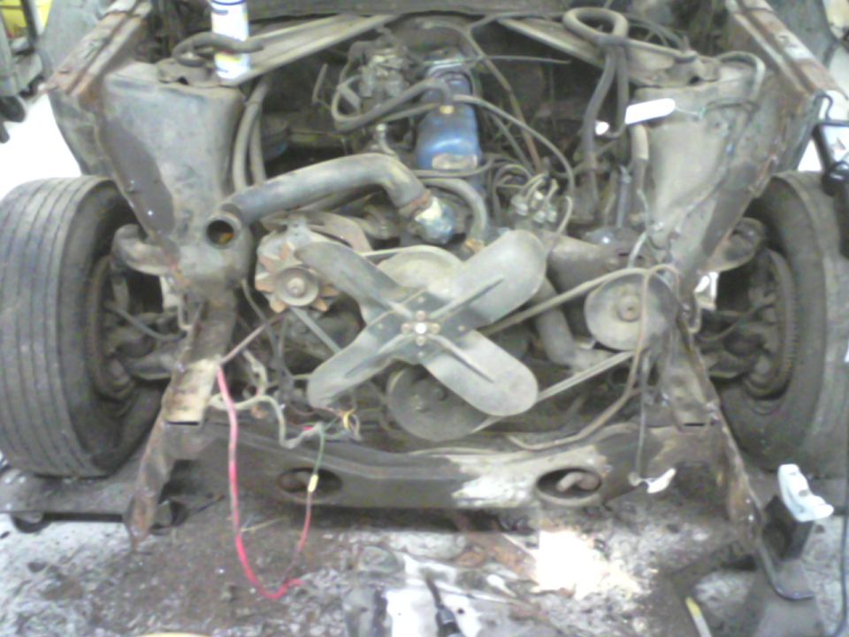 car engine bay with fan and belts visible, front end disassembled