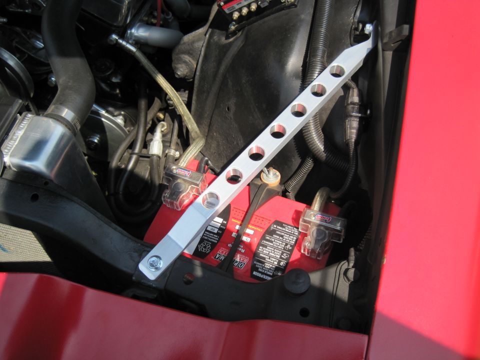 Red car engine bay with a red battery and a silver strut bar
