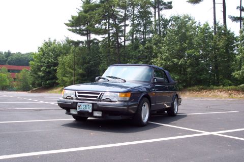 2001 Ford Crown Victoria - A dark blue convertible is parked in an asphalt lot with white lines, surrounded by trees.