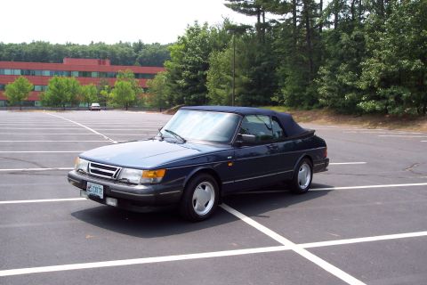 2001 Ford Crown Victoria - A dark blue 1992 Saab 900 Turbo Convertible is parked in a large, empty asphalt lot with a building and trees in the background.