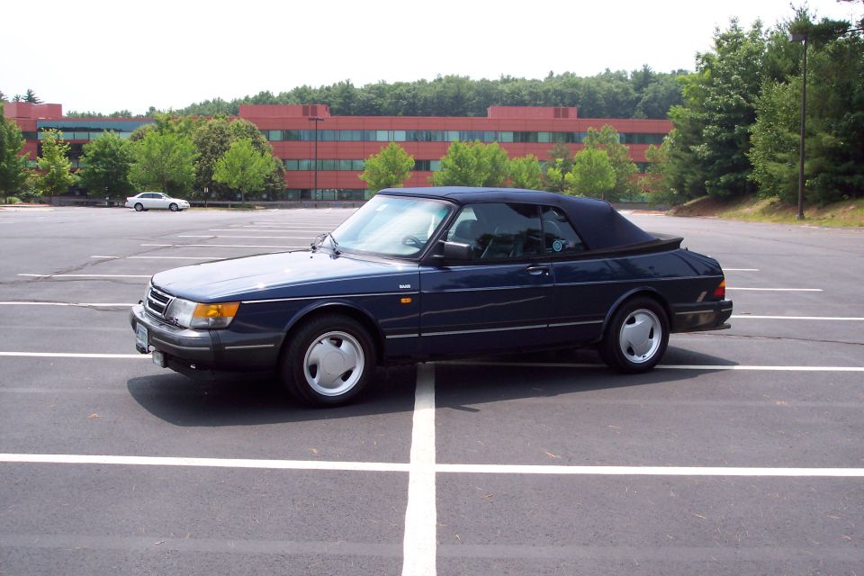 Dark blue Saab 900 convertible parked in a lot with a white car in the background