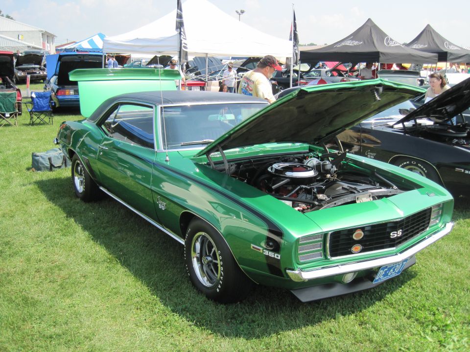 Green 1969 Chevrolet Camaro SS with hood open, parked on grass at an outdoor event