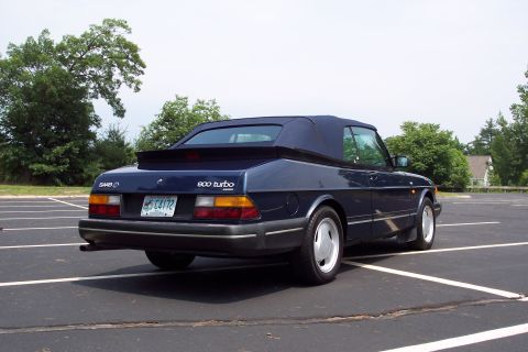 2001 Ford Crown Victoria - A dark blue Saab 900 Turbo convertible is parked in a lot with trees and a house in the background.