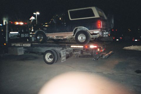 1994 Ford Bronco - A dark blue SUV, likely a 1992 Ford Bronco, is loaded onto a tow truck at night.