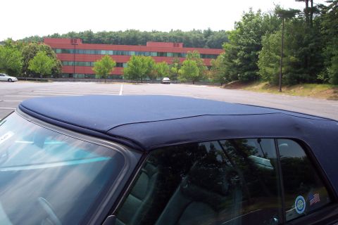 2001 Ford Crown Victoria - The top of a dark blue convertible is shown in the foreground, with a parking lot and building behind it.
