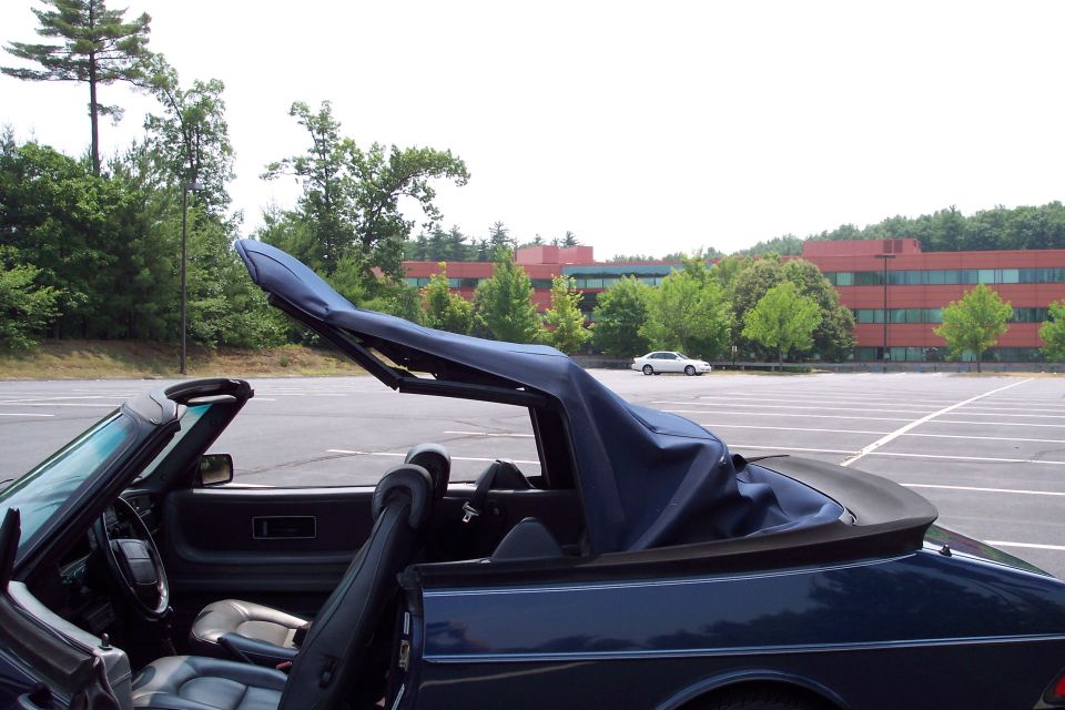Dark blue convertible interior with top partially down, white car in background