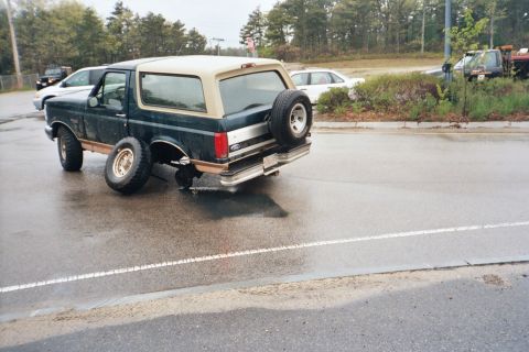 1994 Ford Bronco - A Ford Bronco, likely from the early to mid-1990s, sits with its rear axle damaged and a wheel detached.