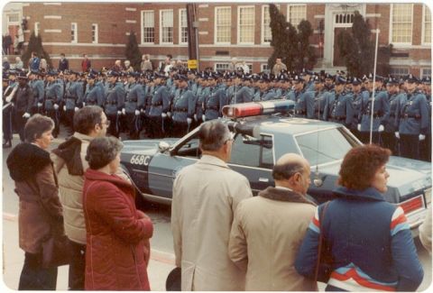 2001 Ford Crown Victoria - A police car is parked in front of a formation of uniformed officers.