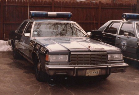 2001 Ford Crown Victoria - A police car with a light bar is parked next to another police car.