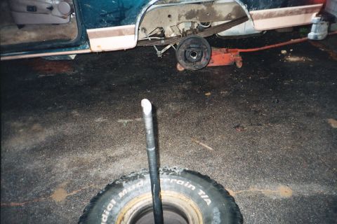 1994 Ford Bronco - A teal and tan SUV is shown with its rear axle removed and a tire lying on the ground, suggesting repairs or maintenance.