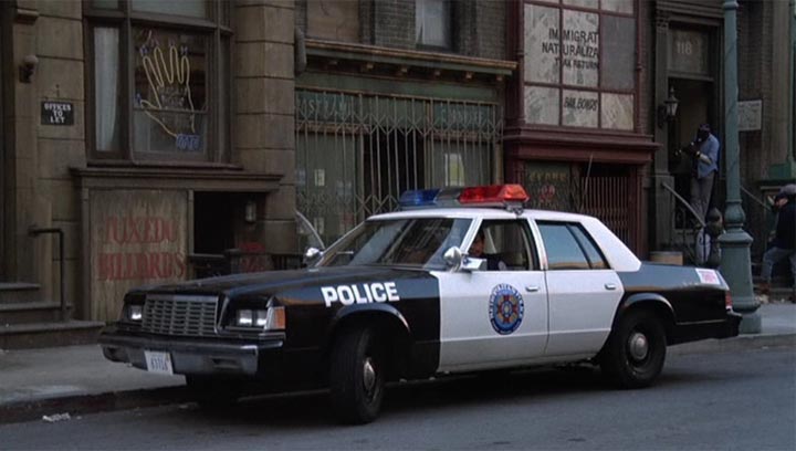 Black and white police car parked curbside, showing "POLICE" text and a departmental seal